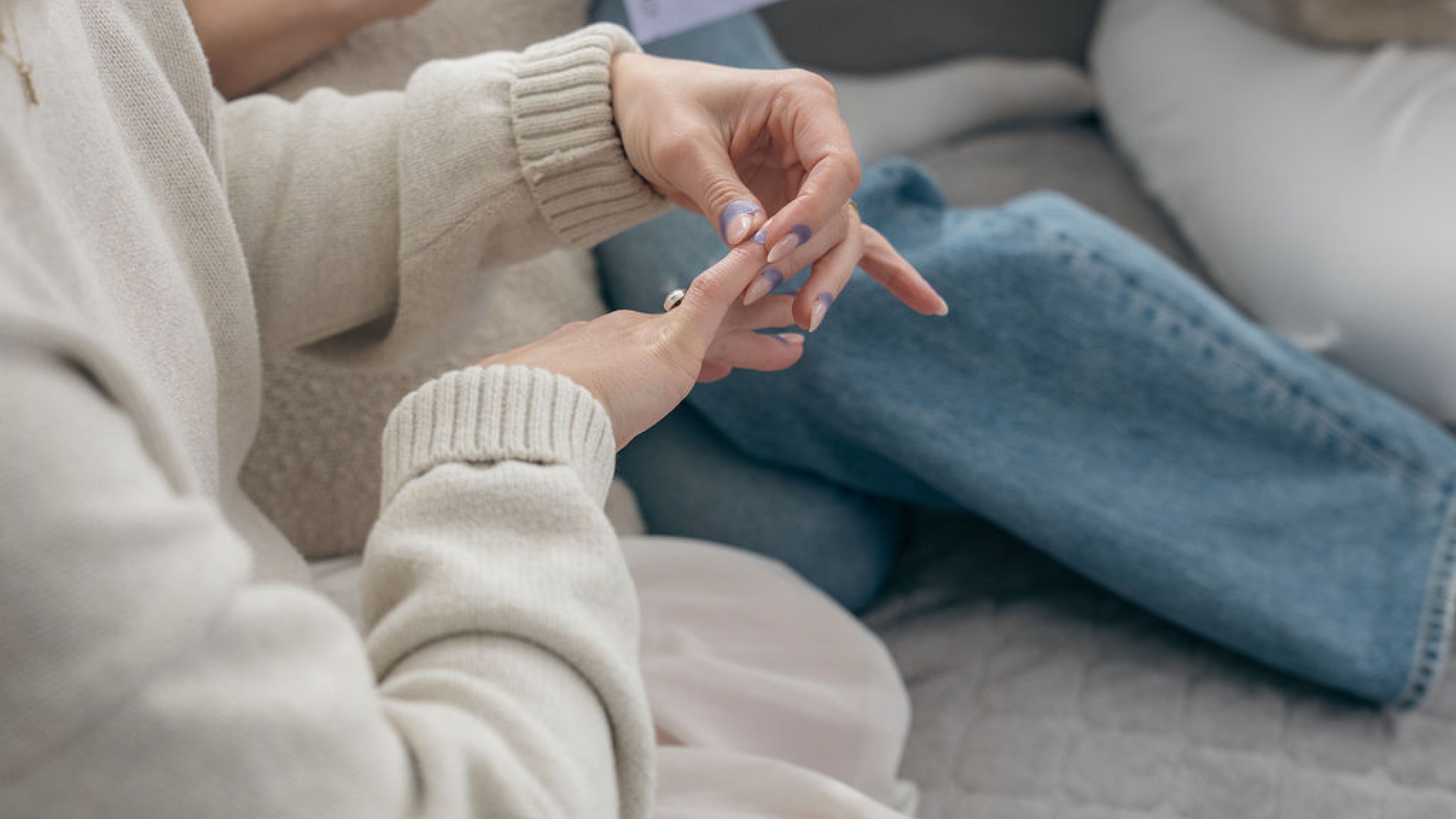 Close-up of two people sitting together, one wearing a beige sweater and the other in blue jeans, with one of them putting cuticle patches onto her fingers.
