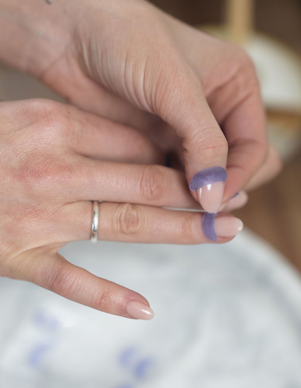 Close-up of hands with French Lilac Cutipatch cuticle patches being placed onto fingers on a blurred background.